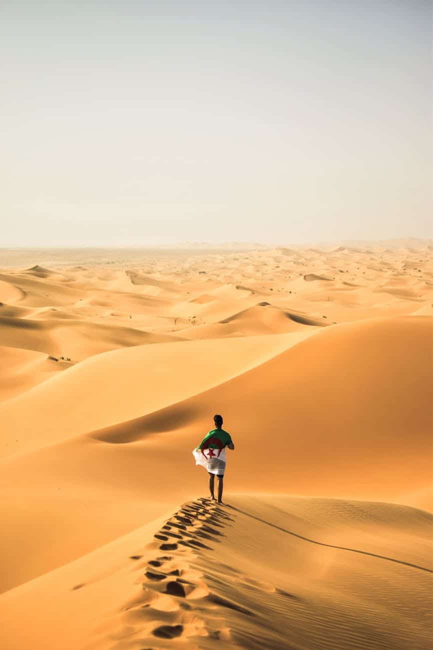 homme qui marche avec un drapeau algérien sur une dune